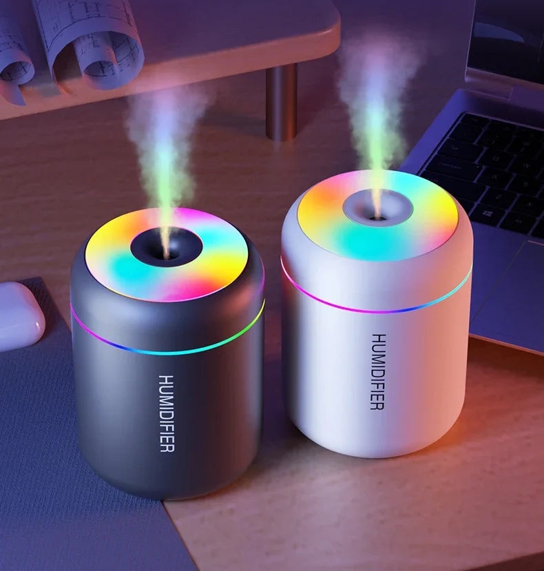 Two humidifiers emitting mist on a desk with a blurred background